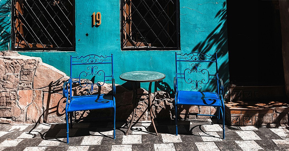 Two chairs outside a sun drenched cafe, with bright blue walls and the number 19